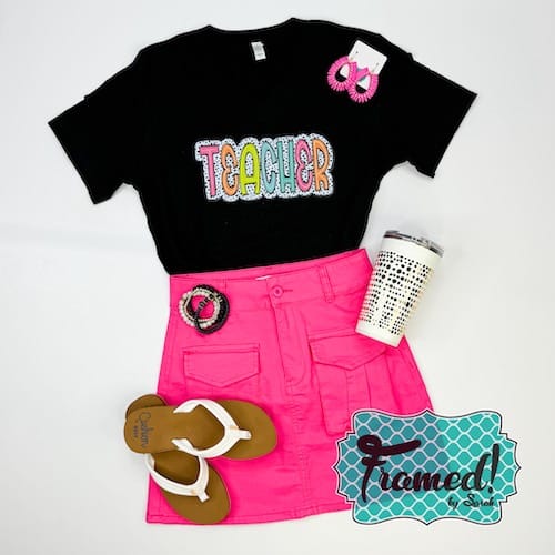 black tshirt with colorful "teacher" graphic styled with hot pink skirt, white sandals, leopard tumbler, and coordinating accessories