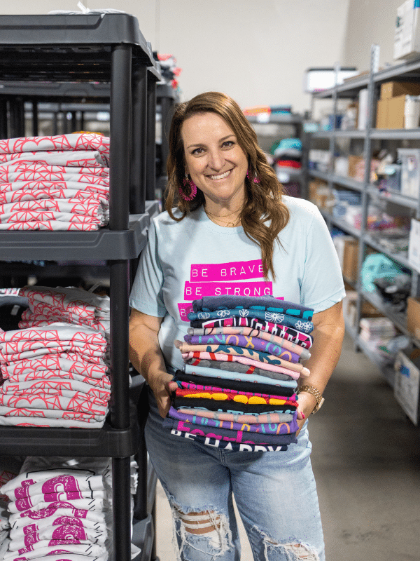 Sarah Williams in a product warehouse holding a stack of graphic tees