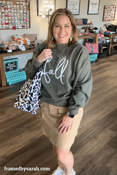 woman wearing green "hello Fall" sweatshirt, khaki cargo skirt, and holding a leopard tote bag