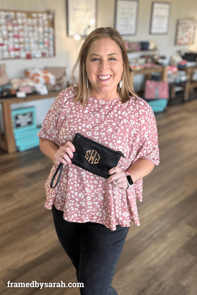 woman wearing mauve leopard print blouse styled with dark wash jeans and monogrammed black wristlet