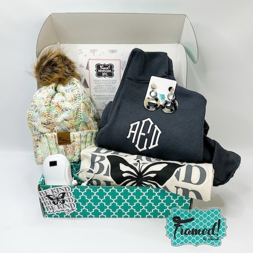 The February 2025 Monogram Box and T-Shirt Club displayed inside an open turquoise box. Contents include: Gray Monogrammed 1/4 zip pullover, multicolor knit beanie, and electric hand warmer plus the ivory "Be Kind Always" t-shirt and matching hoop earrings